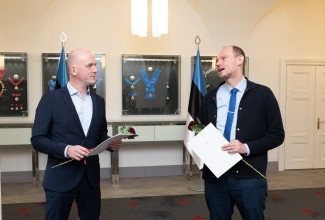 Vasakul Taimar Peterkop, paremal Ott Karulin tänukirjadega Riigikantselei pitsatisaalis. Taustal regaaliad seinal vitriinides.